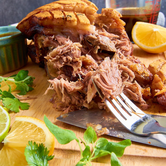 Slow Roasted Cuban Pork Shoulder on a wooden board, tender meat pulled apart, surrounded by oranges