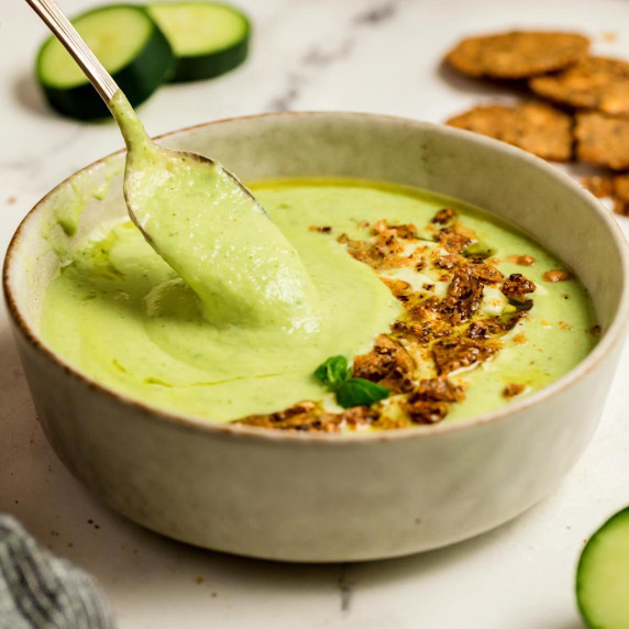 Creamy cucumber gazpacho being lifted with a spoon from a bowl topped with crunchy croutons and oliv