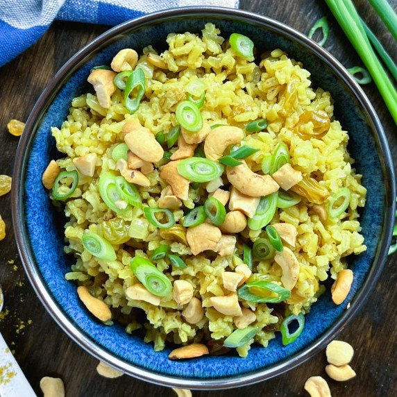 Curried rice with raisins and cashews in a blue bowl topped with sliced green onion.