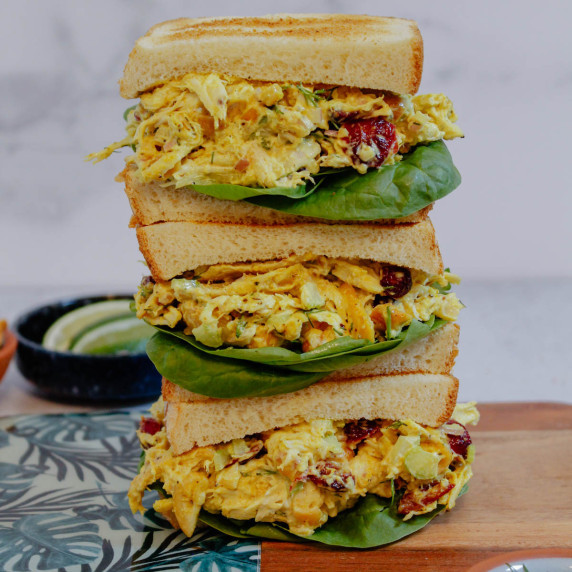 Three stacked curry chicken salad sandwiches on a cutting board.