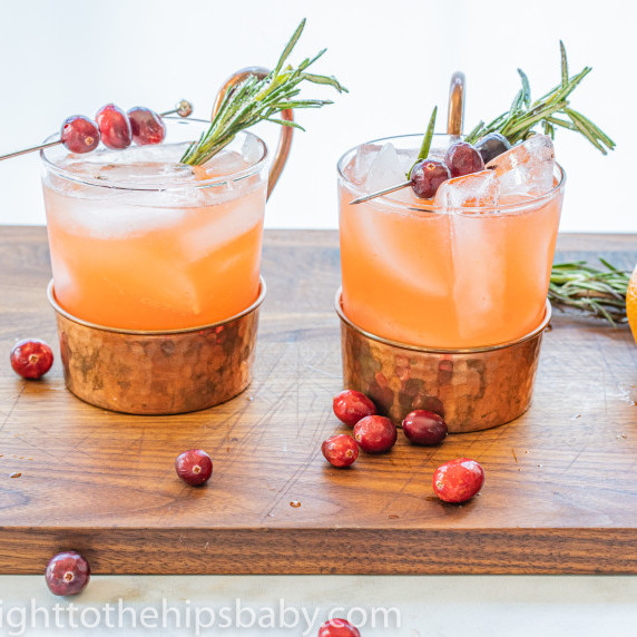 Two cocktail glasses filled with orangey pink Spiced Cranberry Punch with rosemary garnish