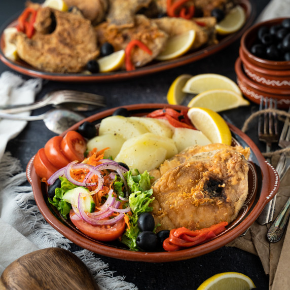 Fried fish, salad and potatoes on a red clay plate