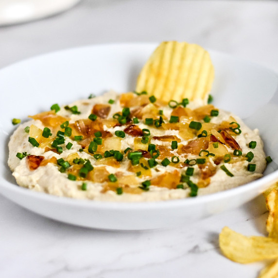 A white bowl with vegan caramelized onion dip and topped with onions and chives.