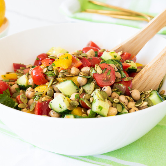 Red Peppers, Tomatoes, Cucumbers, Chickpeas and more combined in a white bowl with a green napkin. 