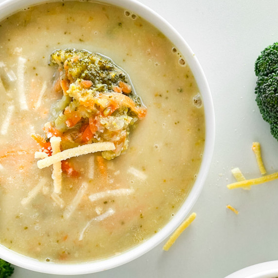 A particular shot of broccoli cheddar soup in a white bowl. Dairy free Cheddar and broccoli garnish.