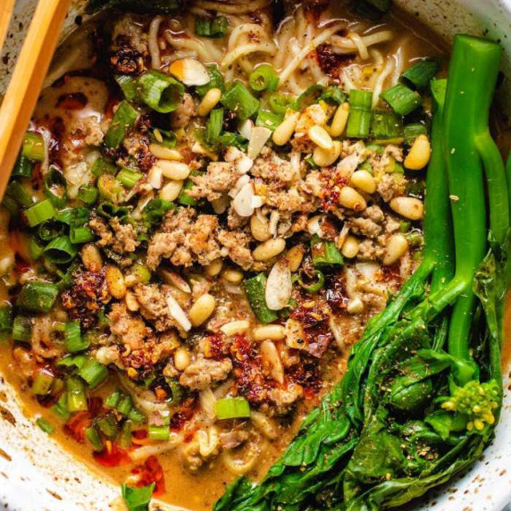 Noodles, soup, pork, garlic cloves and blanched bok choy in a bowl with chopsticks