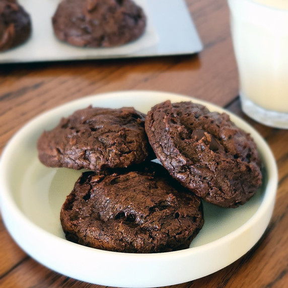 Dark chocolate truffle cookies on a white plate with a glass of milk