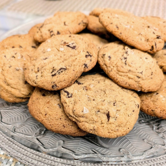 a pile of dark chocolate chip cookies with sea salt on a serving platter at a holiday party