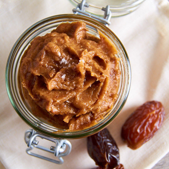 A jar of easy date caramel, topped with flaked sea salt, surrounded by dates.