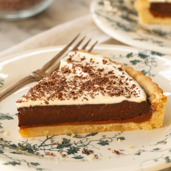 A slice of caramel chocolate tart on a white plate with a fork to the side.