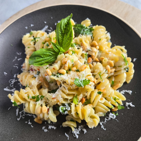 A plate of fusilli topped with toasted pine nuts, green herbs, and grana padano on a matte plate.