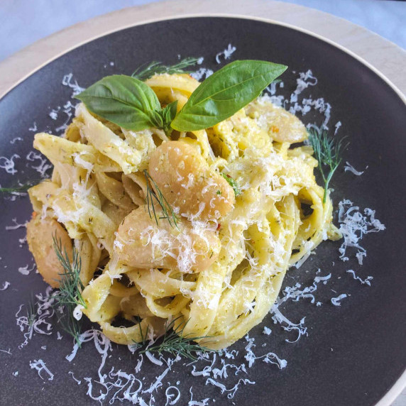 A nest of tagliatelle with butter beans garnished with green herbs on a black plate.