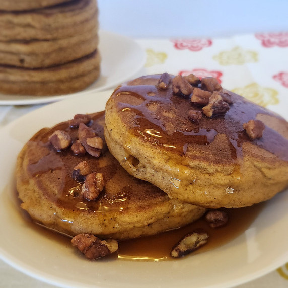 Double pumpkin pancakes on a plate drizzled with syrup and topped with pecans