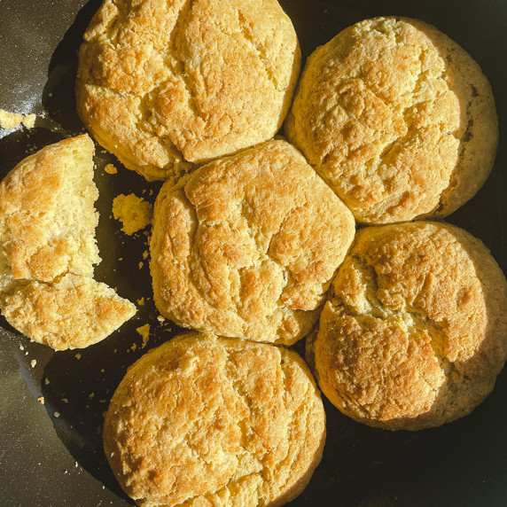 Round biscuits arranged in a large cast-iron pan with one biscuit half eaten.
