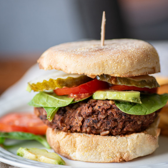 A black bean burger with spinach, tomatoes, avocado, and pickles on a plate.