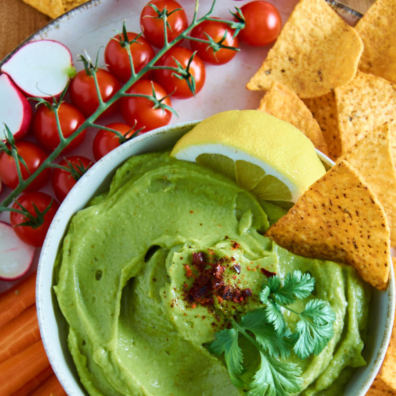 A bowl of easy Guacamole surrounded by tortilla chips and crudites