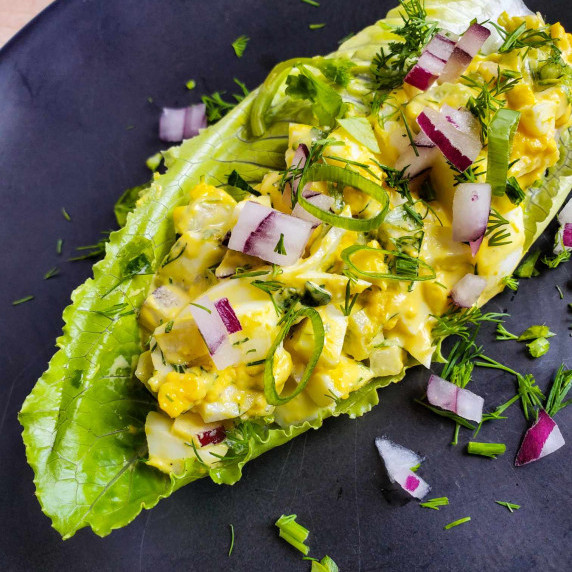 A green lettuce cup stuffed with creamy, yellow egg salad on a black plate.
