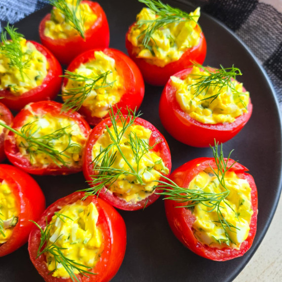 Bright red tomatoes stuffed with creamy yellow egg salad on a black plate