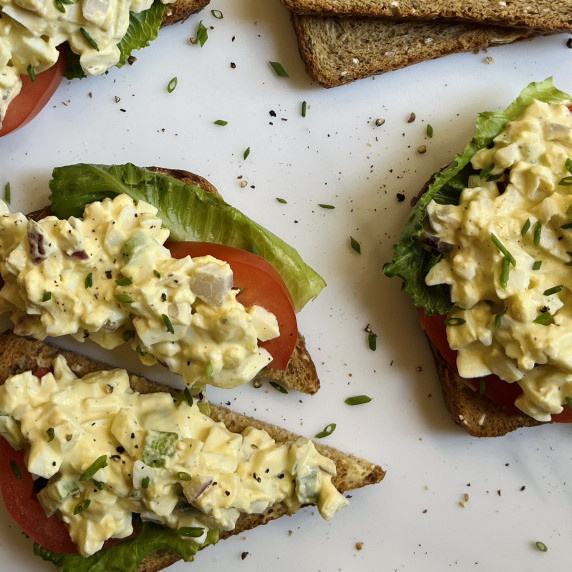 Egg salad on top of whole grain bread garnished with lettuce and tomato slices.