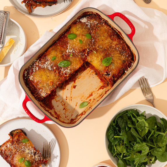 A dish of eggplant parmigiana on a table with pieces taken out and on surrounding plates