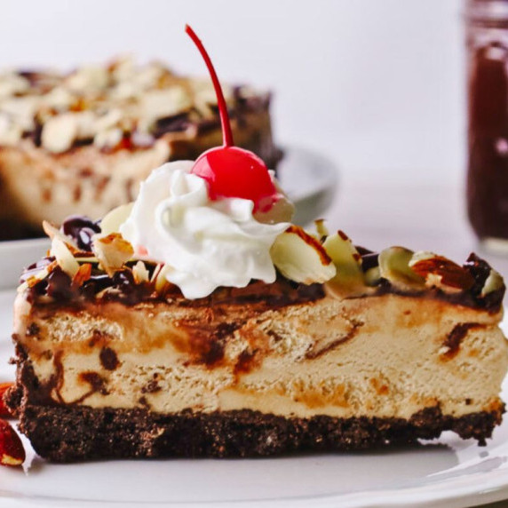 a slice of mocha almond fudge pie with whipped cream and a cherry on top. It's on a white plate 
