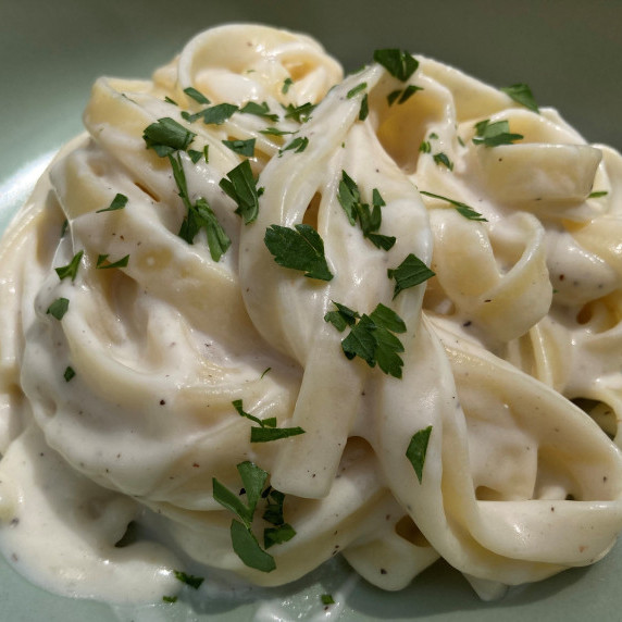 Fettucine topped with fresh minced parsley in a blue bowl.