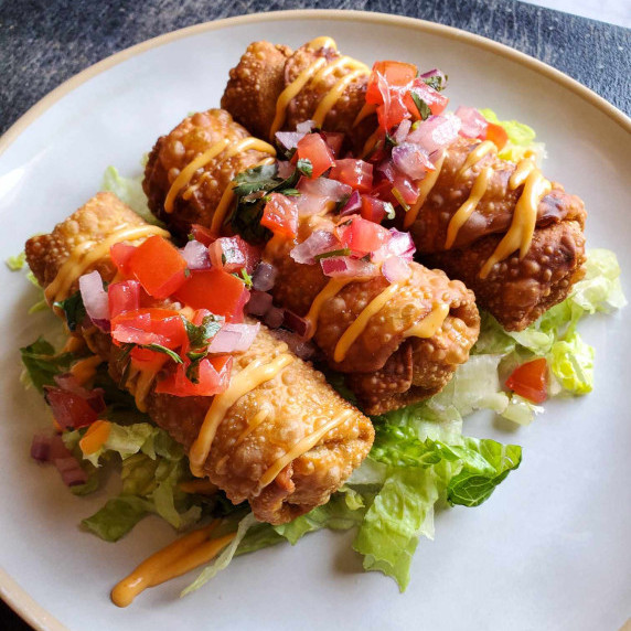 Crispy, golden brown egg rolls dressed in colourful pico on a bed of green romaine.