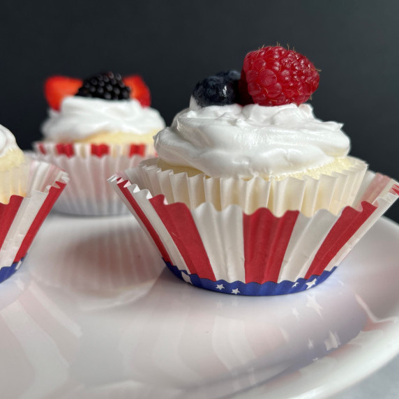 Cupcakes topped with white frosting and fresh strawberries and blackberries on a white platter.