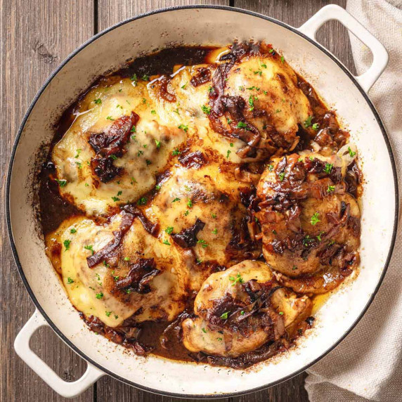 A skillet filled with French onion chicken thighs, topped with caramelized onions & cheese