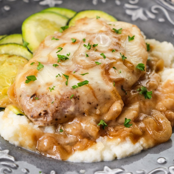 Pork chop smothered in onions, gravy, and cheese on a bed of mashed potatoes.