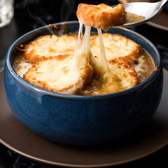 A spoonful of soup pulling out a cheese crouton from the top of the bowl.