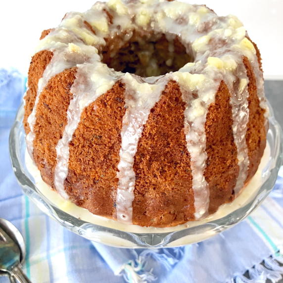 Bundt cake with drizzle down the sides, on a glass plate, on top of a blue cloth