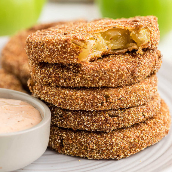 A stack of fried green tomatoes, with the top one missing a bite.