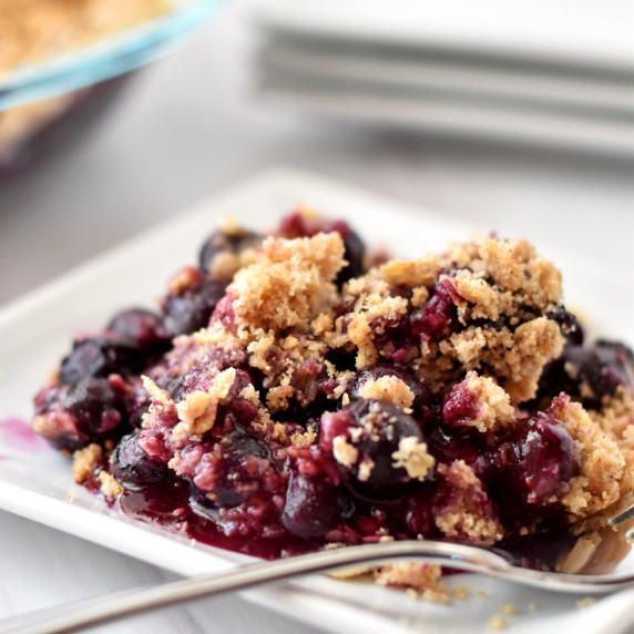 Serving of gluten free blueberry crisp and fork on small white plate.
