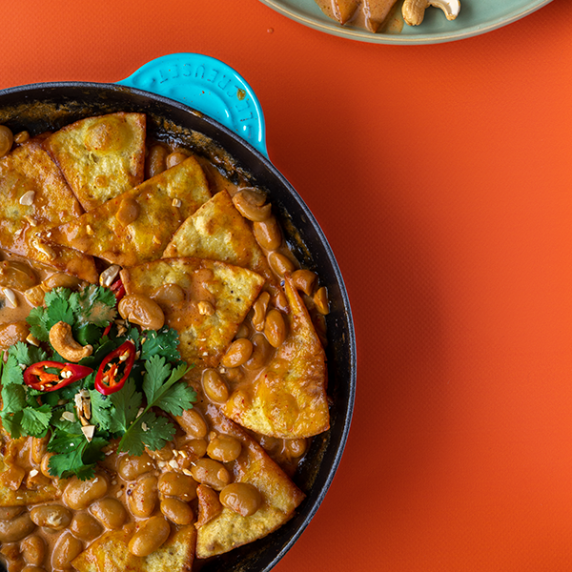 A large blue skillet filled with butterbean penang curry chilaquiles on a bright orange background.