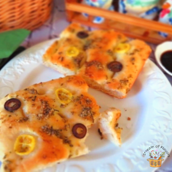 Focaccia bread with tomatoes and olive on a white plate with balsamic vinegar and olive oil