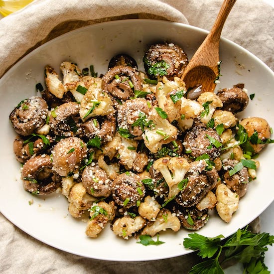 Garlic mushrooms with cauliflower crumbles and parsley and wooden spoon on a white plate