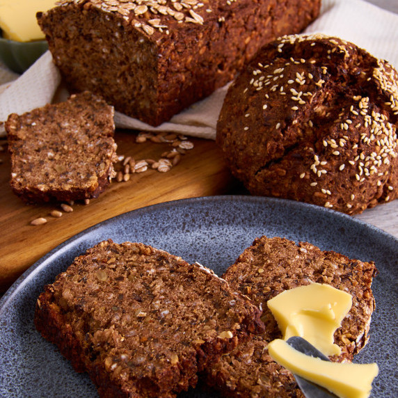 2 loafs of German Sourdough Black Bread. A plate in the front with slices on it, topped with butter