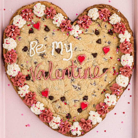 A giant heart shaped cookie with pink and white frosting and words piped saying be my valentine.