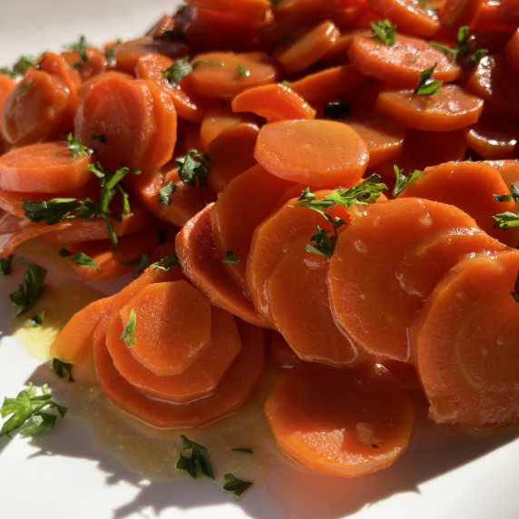 Glazed sliced carrots in a white bowl topped with minced fresh parsley.