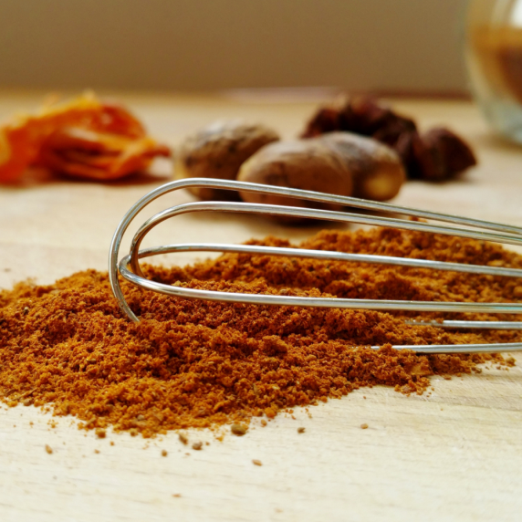 Pile of gingerbread spice beneath a whisk, with whole spices behind.