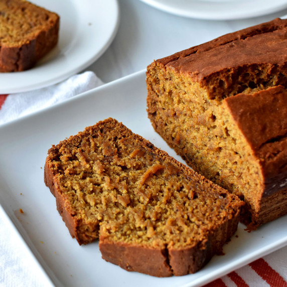 1 slice of gluten free pumpkin banana bread and loaf on white serving plate.