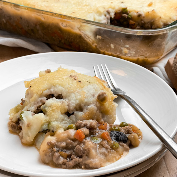 shepherd's pie on a white plate with a fork. The casserole in the background.