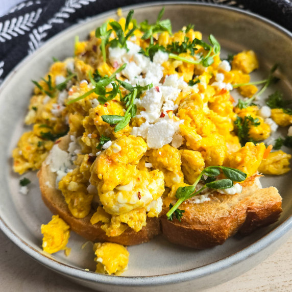Golden brown toast topped with fluffy yellow scramble and pops of white feta & greens