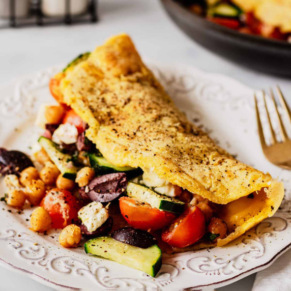 Loaded Greek omelette with tomatoes, feta, chickpeas, and cucumber on a white plate