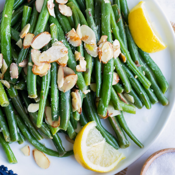 Green Beans Almondine RECIPE placed on a white plate topped with slivered almonds and lemon slices.