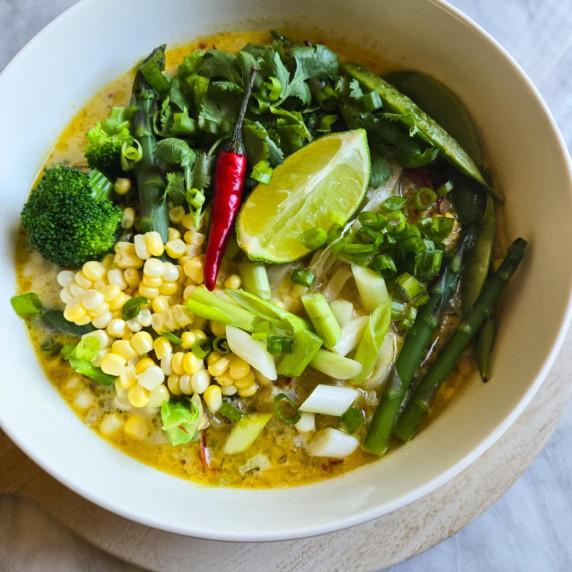 A vibrant bowl of green curry with green veggies, yellow corn, and a red chili.