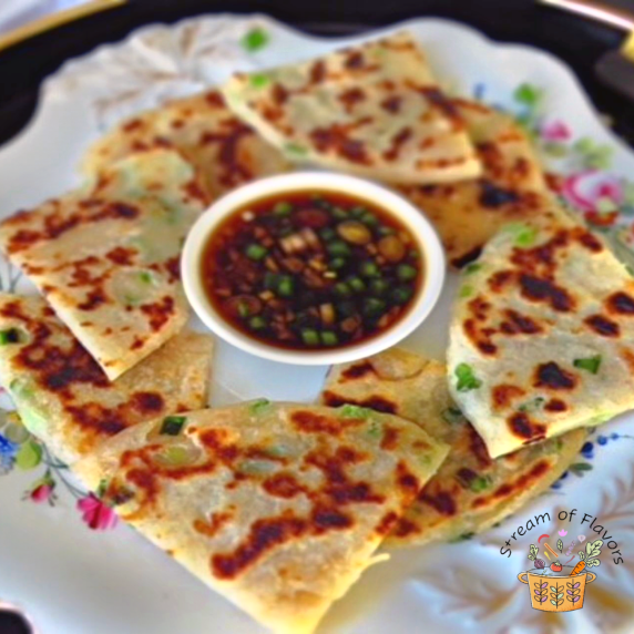 Green onion pancake triangles in a circle with homemade brown sauce in the center of a plate