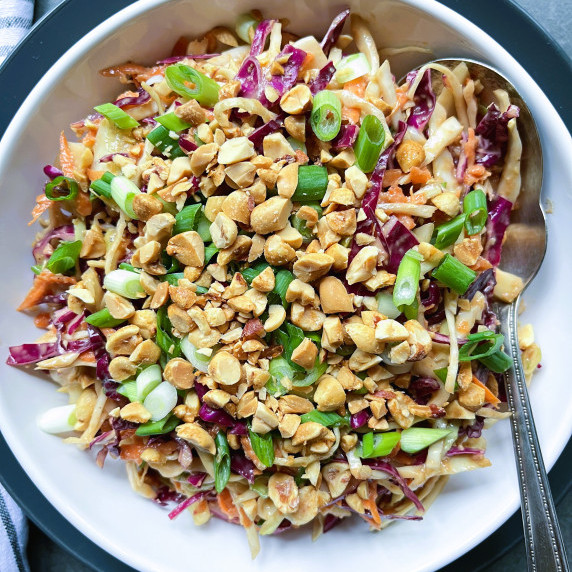 Green and red cabbage slaw garnished with peanuts and green onion in a white bowl. 