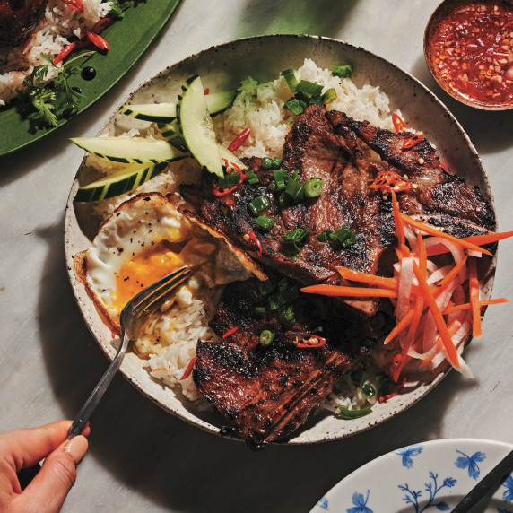 Grilled pork chops over rice with a fried egg, pickled veggies, cucumbers, and dipping sauce.